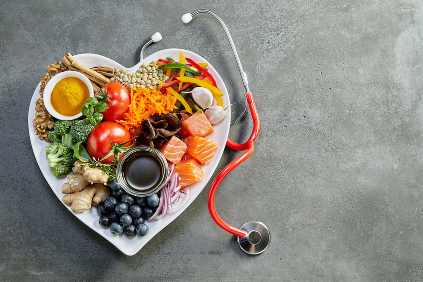 Fresh food for a healthy heart with acai, lentils, soy sauce, ginger, salmon, carrot, tomato, turmeric, cinnamon, walnuts, garlic, peppers, broccoli, basil, onion with a stethoscope